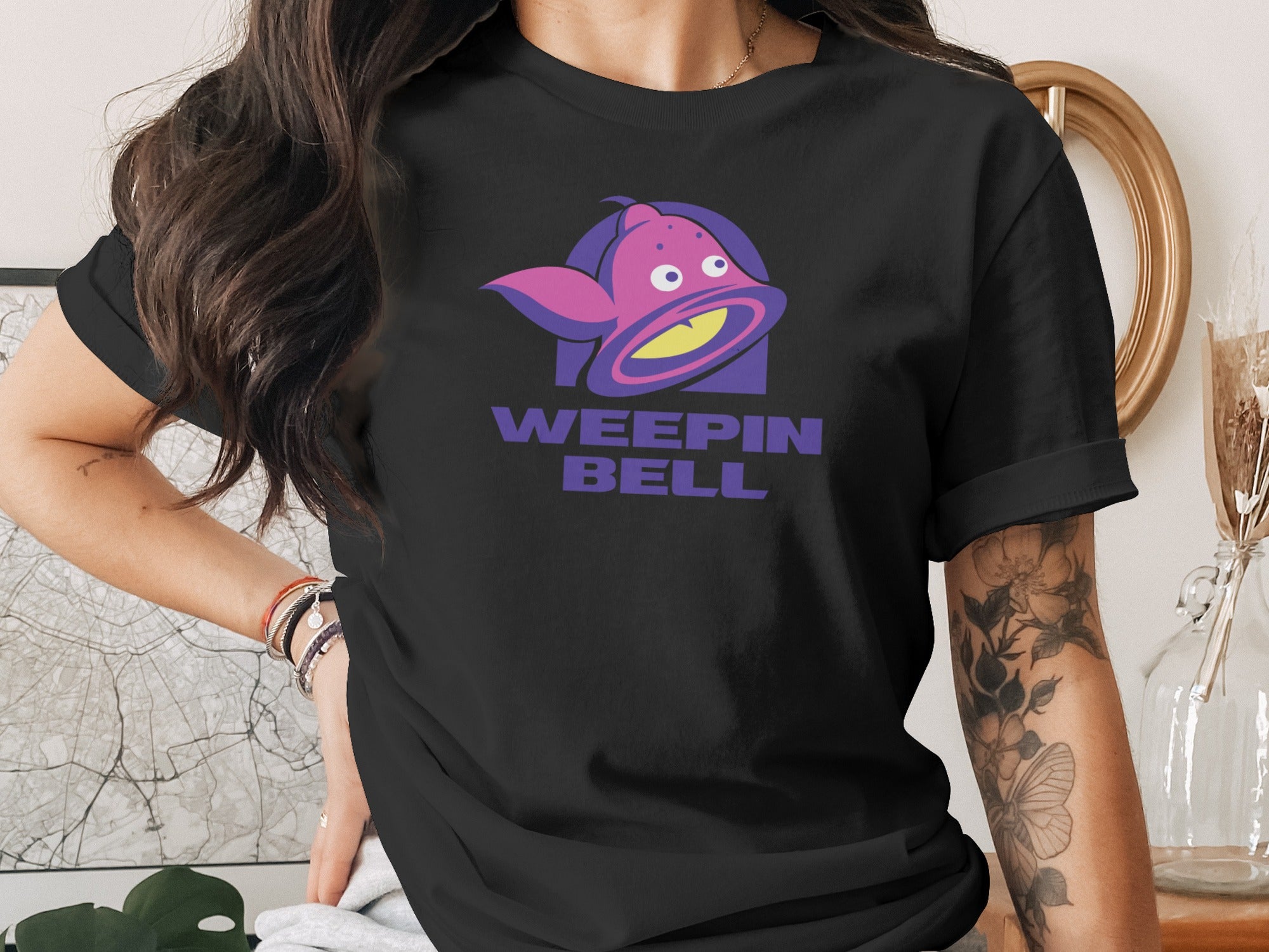 Black t-shirt with "Weepin' Bell" logo featuring a purple, cartoonish bell character.