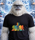 Yeti wearing a t-shirt with colorful Bigfoot silhouettes crossing a road.