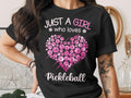 Black t-shirt with pink pickleball heart graphic and text "JUST A GIRL * who loves * Pickleball".