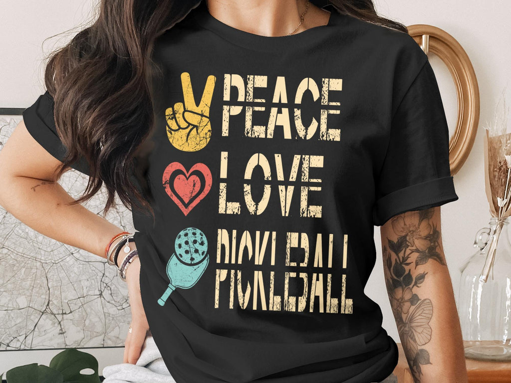 Black t-shirt with "Peace Love Pickleball" text and peace sign, heart, and pickleball graphic.