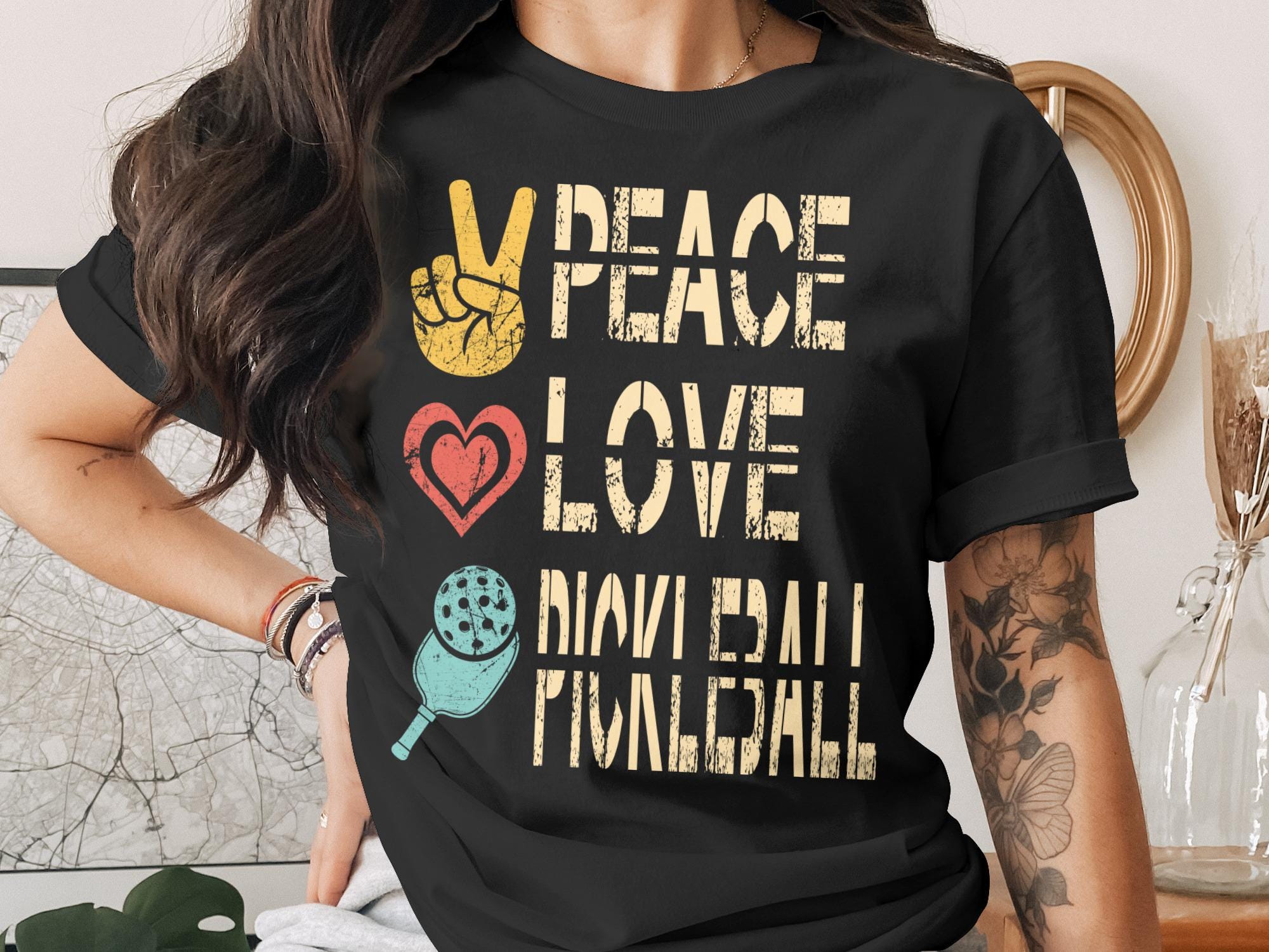 Black t-shirt with "Peace Love Pickleball" text and peace sign, heart, and pickleball graphic.
