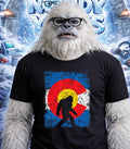 Yeti wearing a t-shirt with a distressed Colorado flag and Bigfoot silhouette.