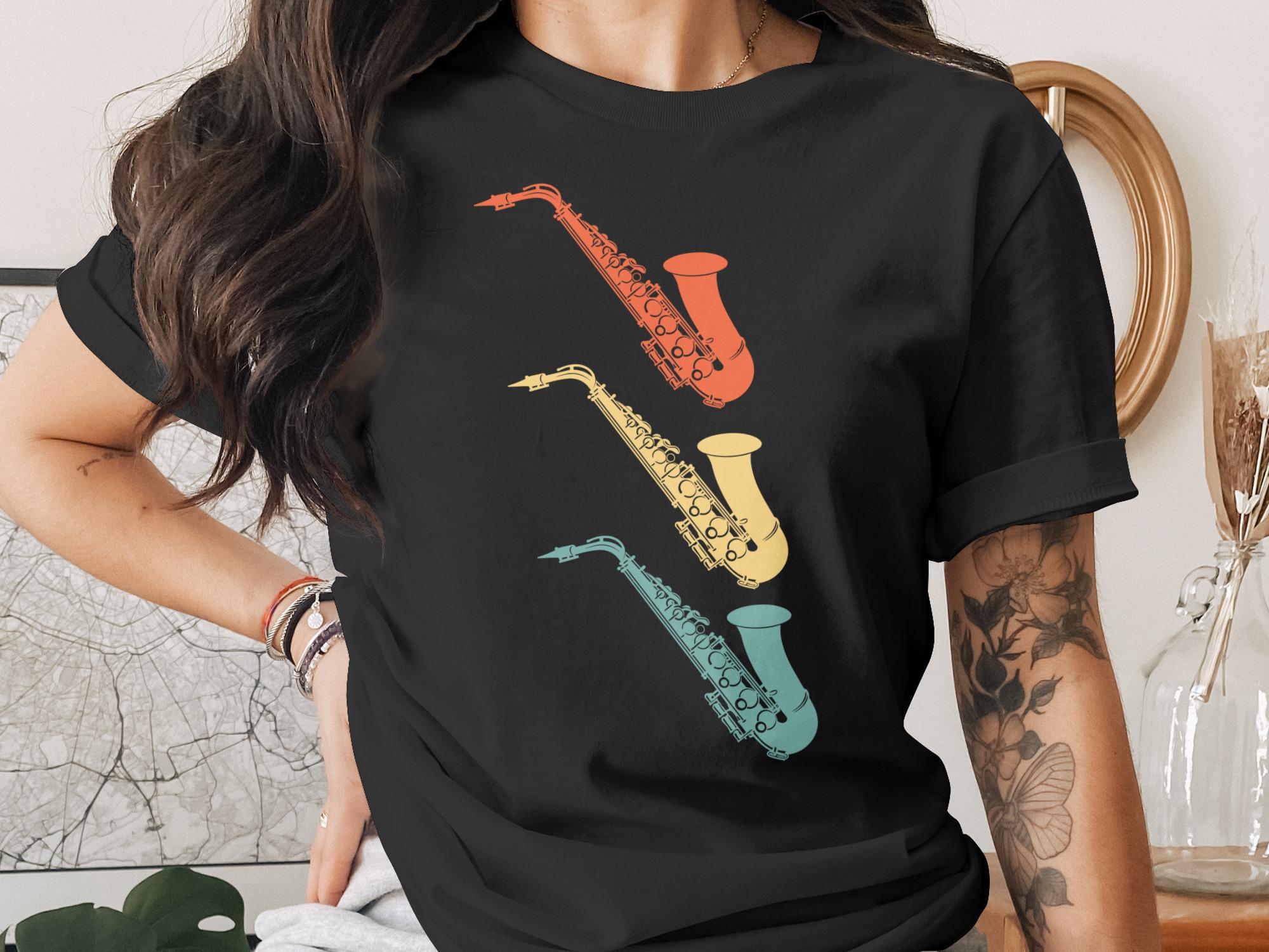 Three retro saxophones in red, yellow, and blue on a black t-shirt.