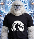 Yeti wearing glasses and a t-shirt with a Bigfoot silhouette against a moon.