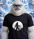 Yeti wearing glasses and a t-shirt with a Bigfoot silhouette against a full moon.