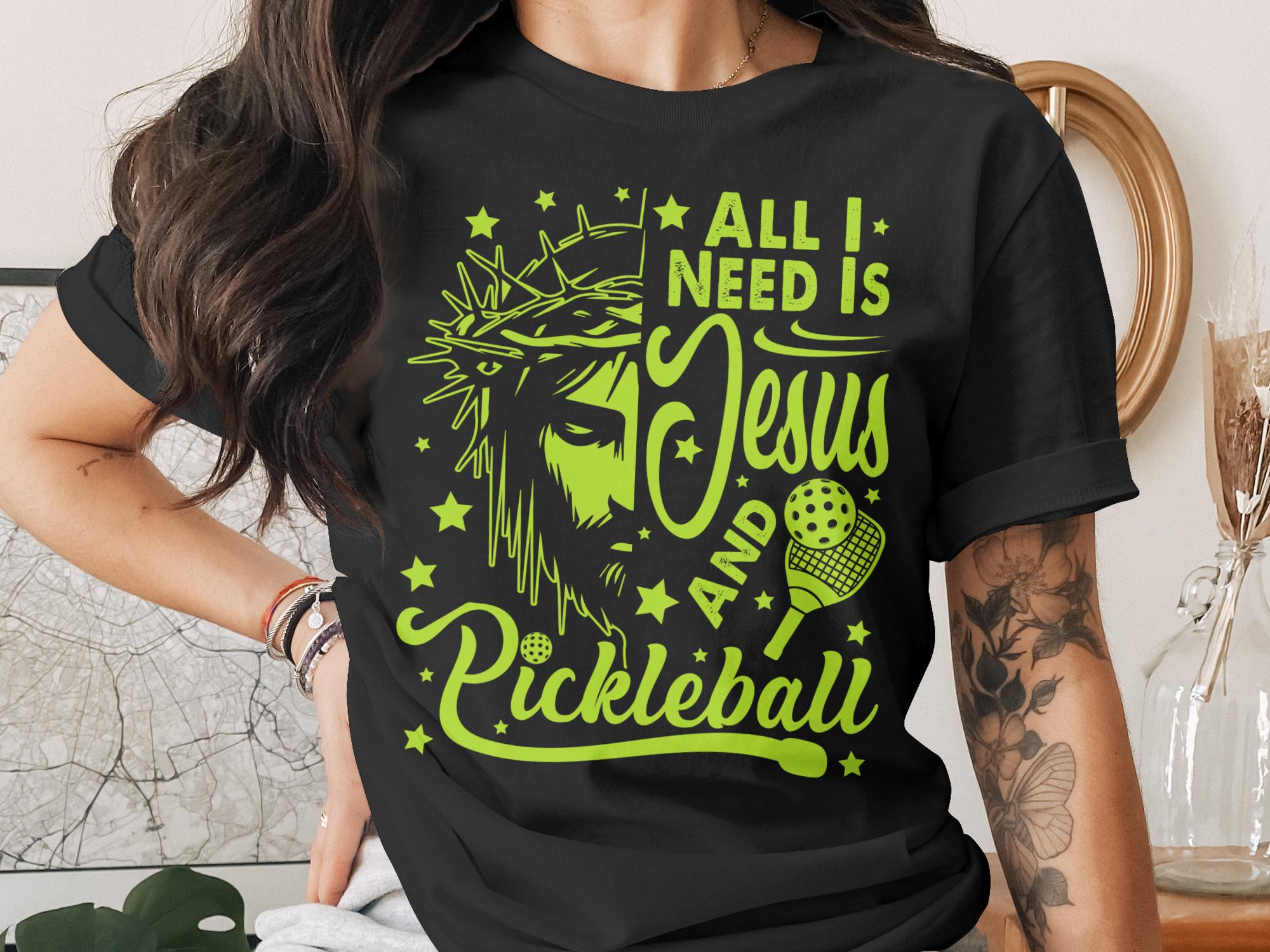 T-shirt with Jesus and pickleball graphic and text "ALL I NEED IS JESUS AND PICKLEBALL".